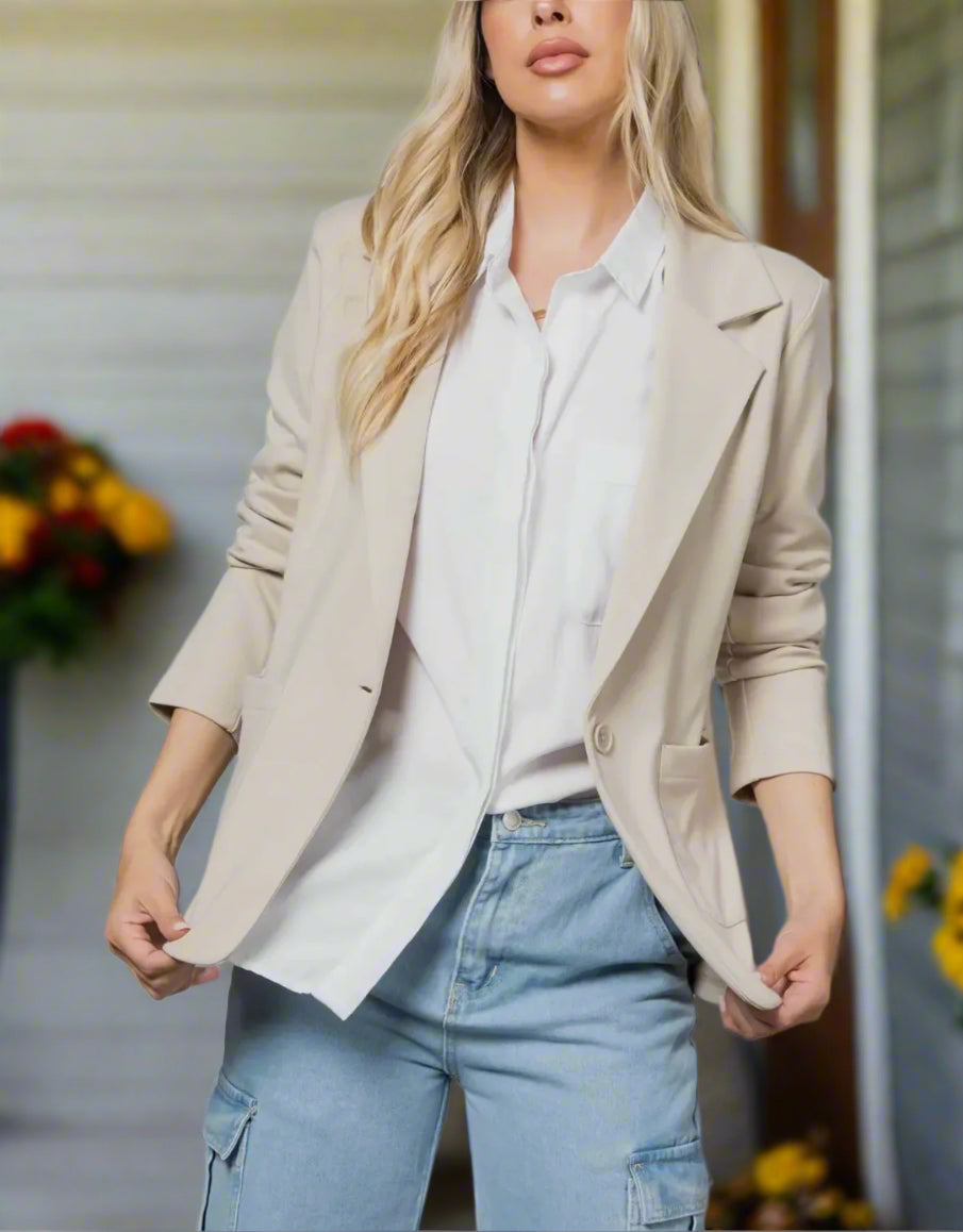 Woman wearing a beige blazer over a white shirt and blue jeans against a neutral background